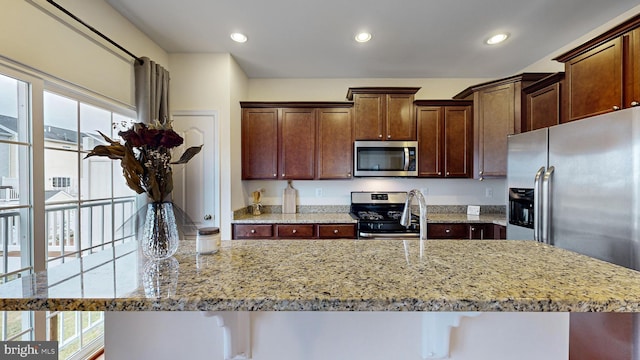 kitchen with light stone countertops, an island with sink, appliances with stainless steel finishes, and a breakfast bar area