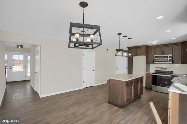 kitchen with pendant lighting, appliances with stainless steel finishes, dark hardwood / wood-style floors, a center island, and light stone counters