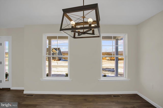 unfurnished dining area featuring a healthy amount of sunlight, dark hardwood / wood-style floors, and a notable chandelier