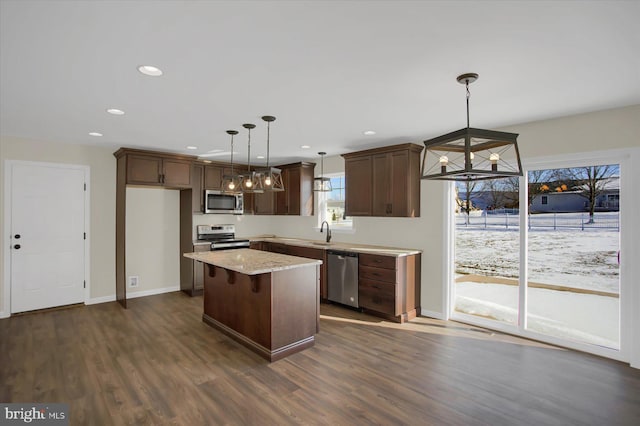 kitchen with pendant lighting, appliances with stainless steel finishes, a center island, light stone counters, and dark hardwood / wood-style flooring