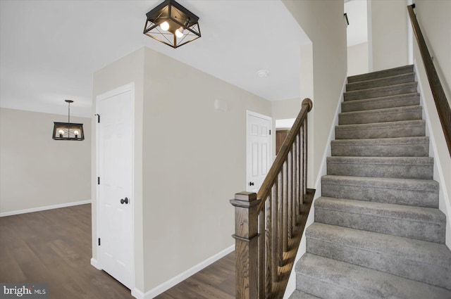 stairway with wood-type flooring and a notable chandelier