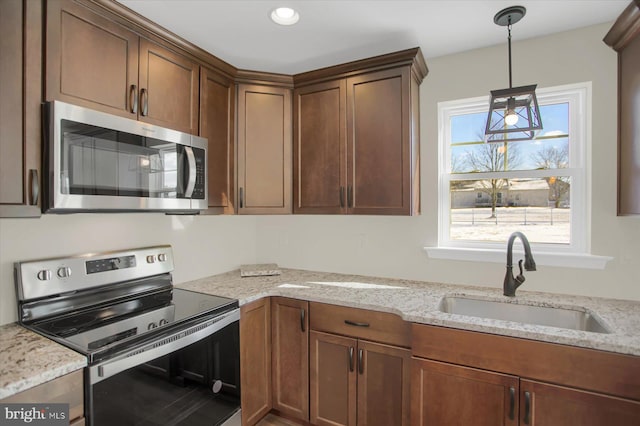 kitchen with light stone counters, stainless steel appliances, decorative light fixtures, and sink