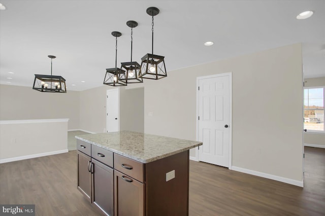 kitchen featuring light stone counters, decorative light fixtures, and dark wood-type flooring