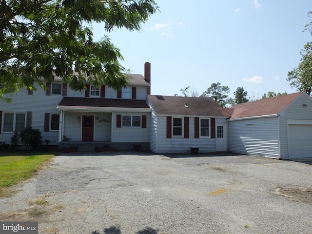 view of front of property with aphalt driveway, a porch, a chimney, and an outbuilding