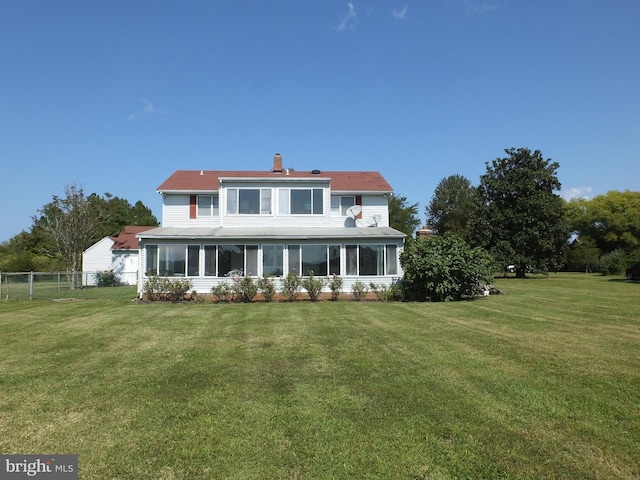 back of property with a sunroom, a chimney, fence, and a lawn
