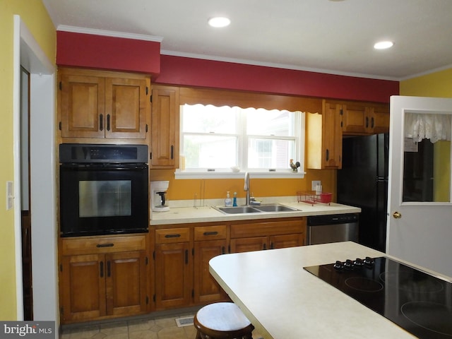 kitchen with a sink, ornamental molding, light countertops, brown cabinetry, and black appliances