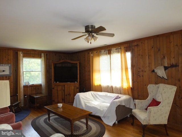 living room featuring wood walls, visible vents, a ceiling fan, and wood finished floors