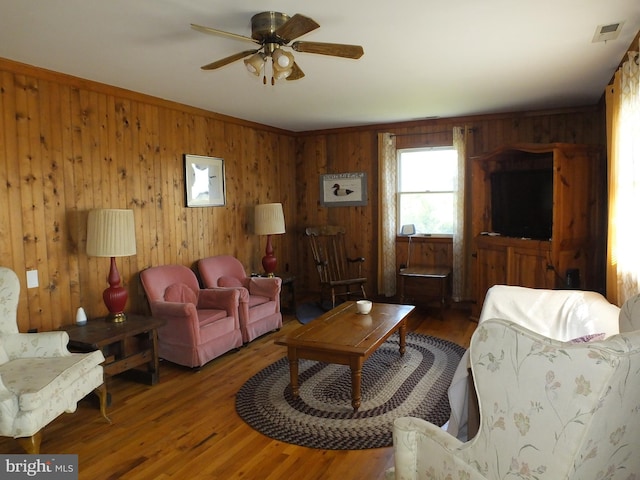 living room with ceiling fan, hardwood / wood-style flooring, wooden walls, and ornamental molding