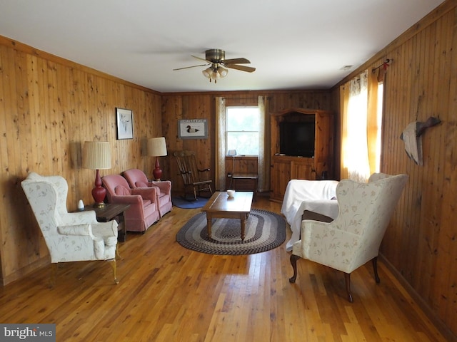 living room with ceiling fan, wood-type flooring, and wooden walls