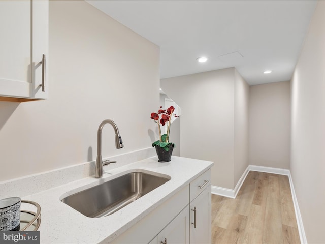 kitchen featuring sink, light hardwood / wood-style floors, light stone counters, and white cabinetry