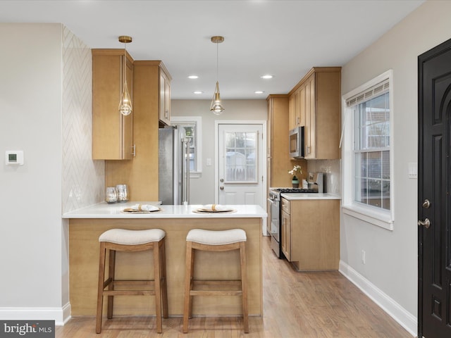 kitchen with tasteful backsplash, light hardwood / wood-style flooring, kitchen peninsula, a healthy amount of sunlight, and appliances with stainless steel finishes