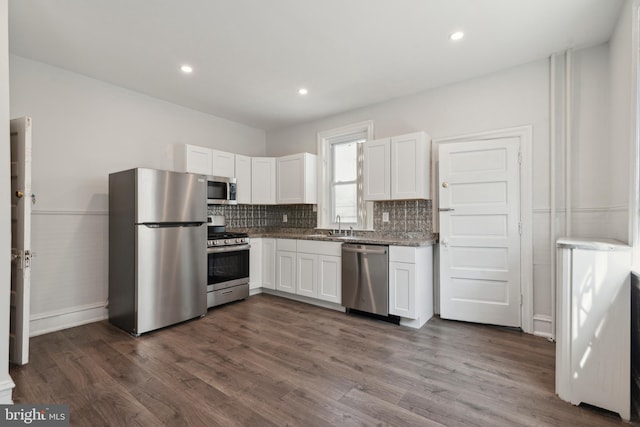 kitchen with light stone counters, dark wood-type flooring, white cabinetry, decorative backsplash, and stainless steel appliances