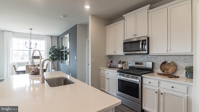 kitchen featuring a chandelier, a kitchen island with sink, sink, white cabinets, and appliances with stainless steel finishes