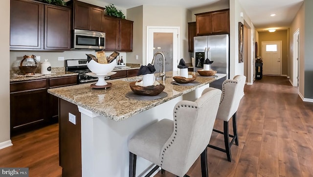 kitchen featuring an island with sink, a kitchen bar, dark hardwood / wood-style flooring, and stainless steel appliances