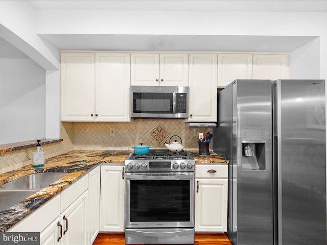 kitchen with appliances with stainless steel finishes, dark stone counters, backsplash, and white cabinets