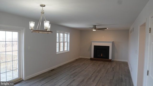 unfurnished living room with ceiling fan with notable chandelier, dark wood-type flooring, and a wealth of natural light