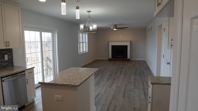 kitchen with light stone countertops, stainless steel dishwasher, decorative light fixtures, a center island, and ceiling fan with notable chandelier