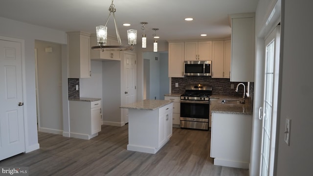 kitchen with sink, decorative light fixtures, white cabinetry, appliances with stainless steel finishes, and a center island