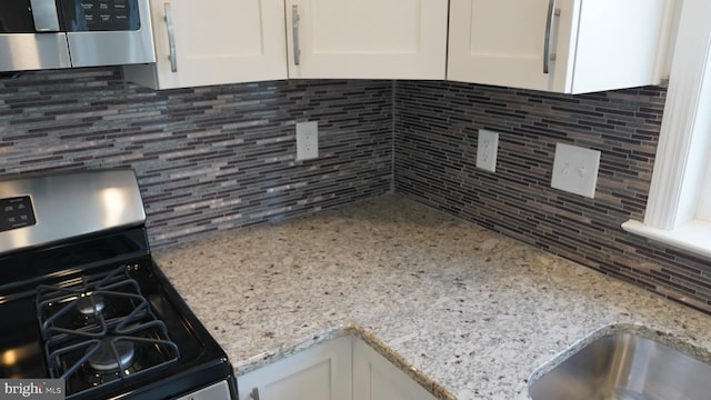 interior details with decorative backsplash, white cabinets, and appliances with stainless steel finishes