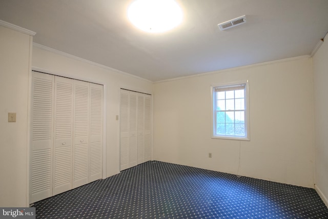 unfurnished bedroom featuring crown molding, carpet, and two closets