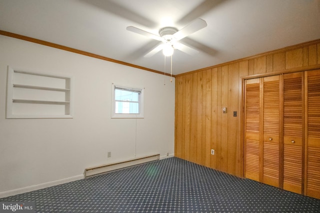 unfurnished bedroom featuring ceiling fan, ornamental molding, wooden walls, baseboard heating, and dark colored carpet