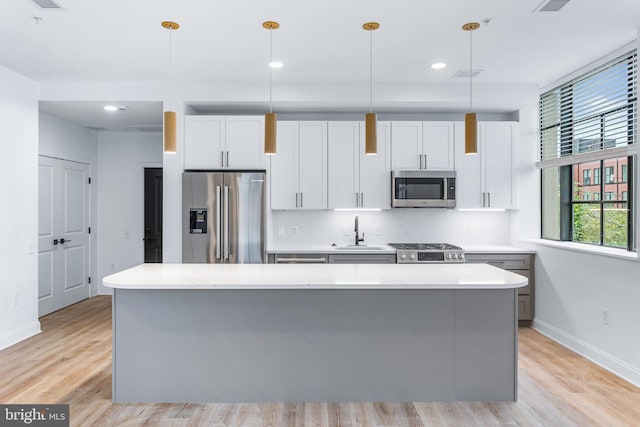 kitchen featuring white cabinets, stainless steel appliances, light hardwood / wood-style floors, and decorative light fixtures