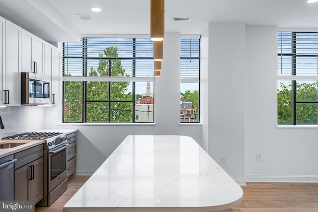 kitchen featuring backsplash, white cabinetry, stainless steel appliances, light stone countertops, and light hardwood / wood-style floors