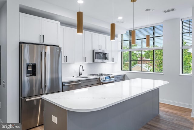 kitchen featuring pendant lighting, appliances with stainless steel finishes, light stone counters, and white cabinets