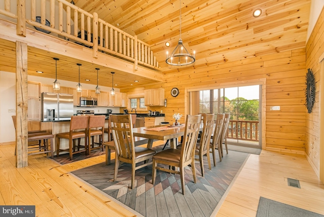 dining room with a high ceiling, wooden walls, an inviting chandelier, and light hardwood / wood-style flooring