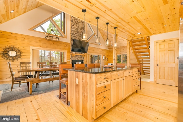 kitchen with vaulted ceiling with skylight, light hardwood / wood-style floors, light brown cabinets, decorative light fixtures, and a stone fireplace