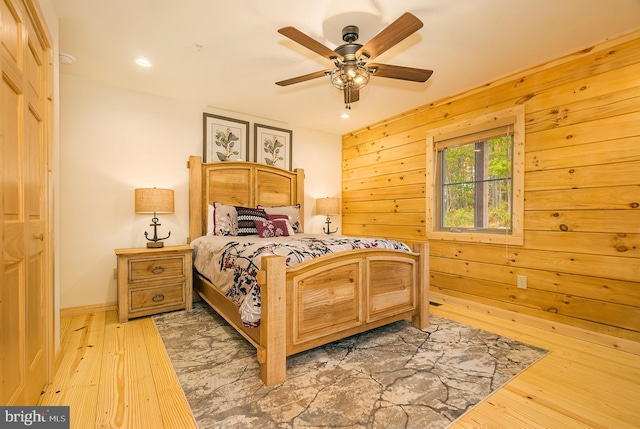 bedroom with wood walls, hardwood / wood-style floors, and ceiling fan