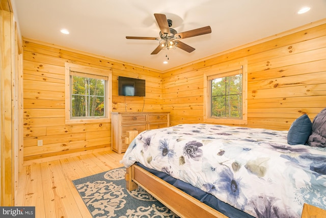 bedroom with ceiling fan, wood walls, hardwood / wood-style floors, and multiple windows