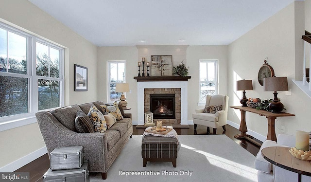 living room with a stone fireplace, baseboards, and wood finished floors