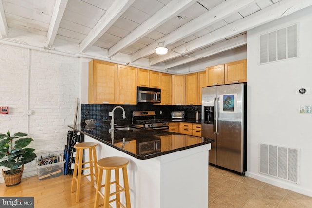 kitchen featuring kitchen peninsula, dark stone counters, brick wall, stainless steel appliances, and sink