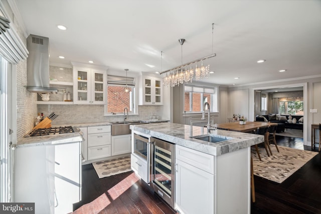 kitchen with dark hardwood / wood-style floors, wall chimney exhaust hood, wine cooler, a center island with sink, and white cabinets