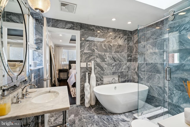 full bathroom with a sink, tile walls, marble finish floor, a freestanding bath, and visible vents