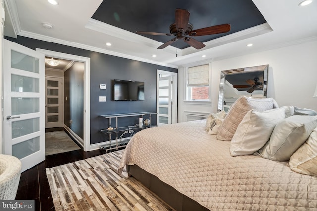 bedroom with crown molding, dark hardwood / wood-style floors, a tray ceiling, and ceiling fan