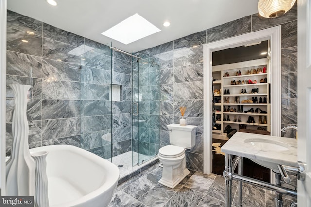 bathroom featuring a shower with door, a skylight, toilet, and tile walls