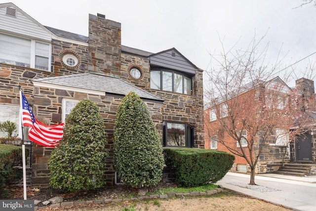 view of front of home featuring stone siding, a chimney, and a high end roof