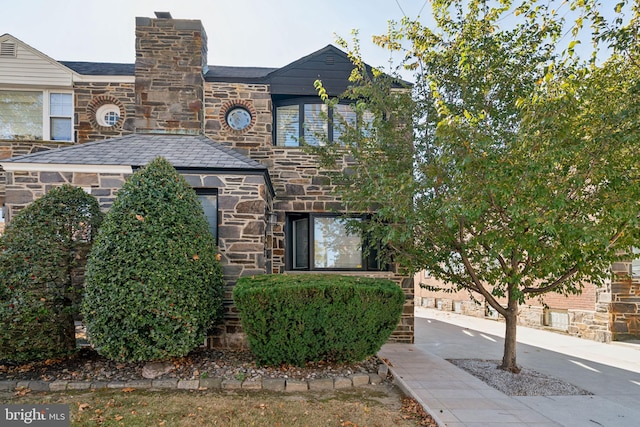 view of front of property featuring a high end roof, stone siding, and a chimney