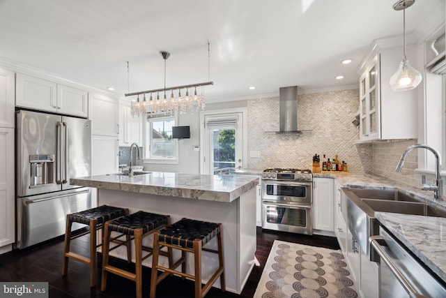 kitchen with wall chimney range hood, crown molding, premium appliances, a sink, and dark wood-style floors