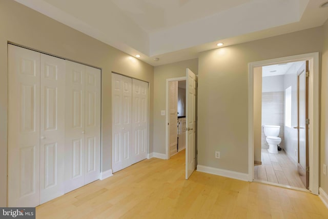 unfurnished bedroom featuring light hardwood / wood-style floors, connected bathroom, and two closets