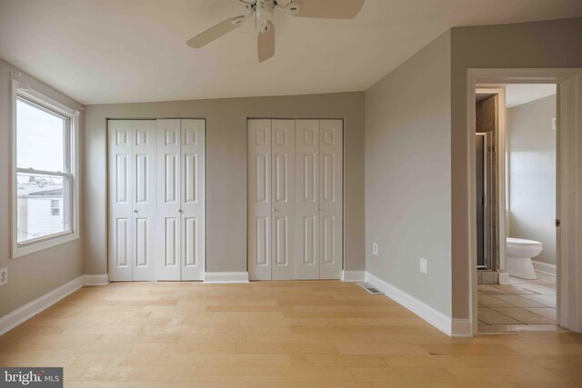 unfurnished bedroom featuring ceiling fan, light hardwood / wood-style floors, ensuite bathroom, two closets, and vaulted ceiling