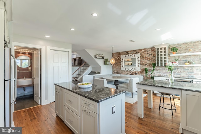 kitchen with dark wood-type flooring, hanging light fixtures, dark stone counters, a center island, and white cabinets