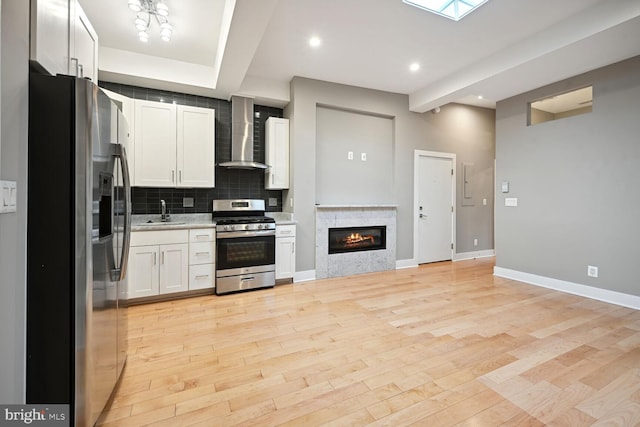 kitchen with white cabinets, appliances with stainless steel finishes, light wood-type flooring, and wall chimney range hood