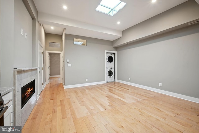 unfurnished living room featuring stacked washer and clothes dryer, light hardwood / wood-style floors, a high end fireplace, and a skylight