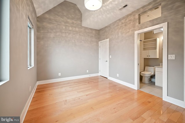 unfurnished bedroom with vaulted ceiling, ensuite bath, and light hardwood / wood-style flooring