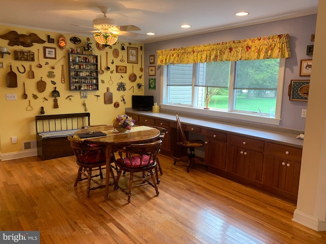 dining area featuring ceiling fan, light wood-type flooring, built in desk, and ornamental molding