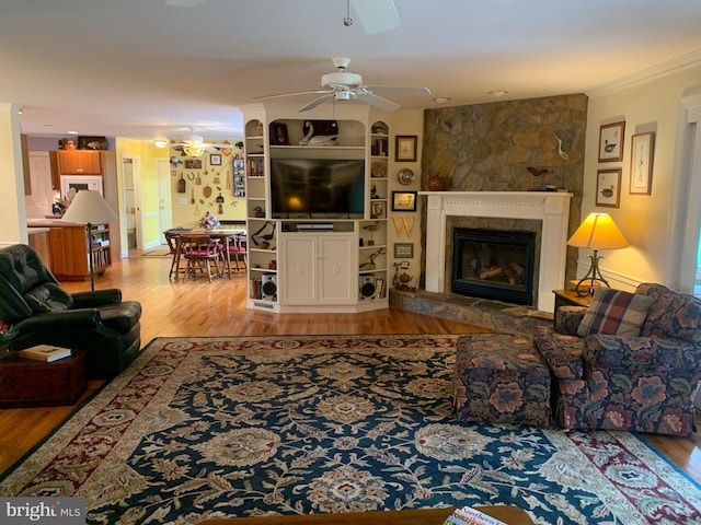 living room with ornamental molding, light wood-type flooring, ceiling fan, and a fireplace