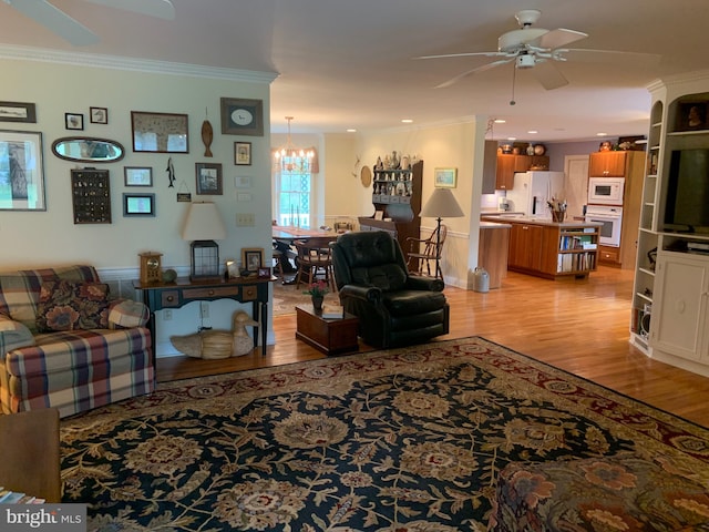 living room with ceiling fan with notable chandelier, ornamental molding, and light hardwood / wood-style flooring